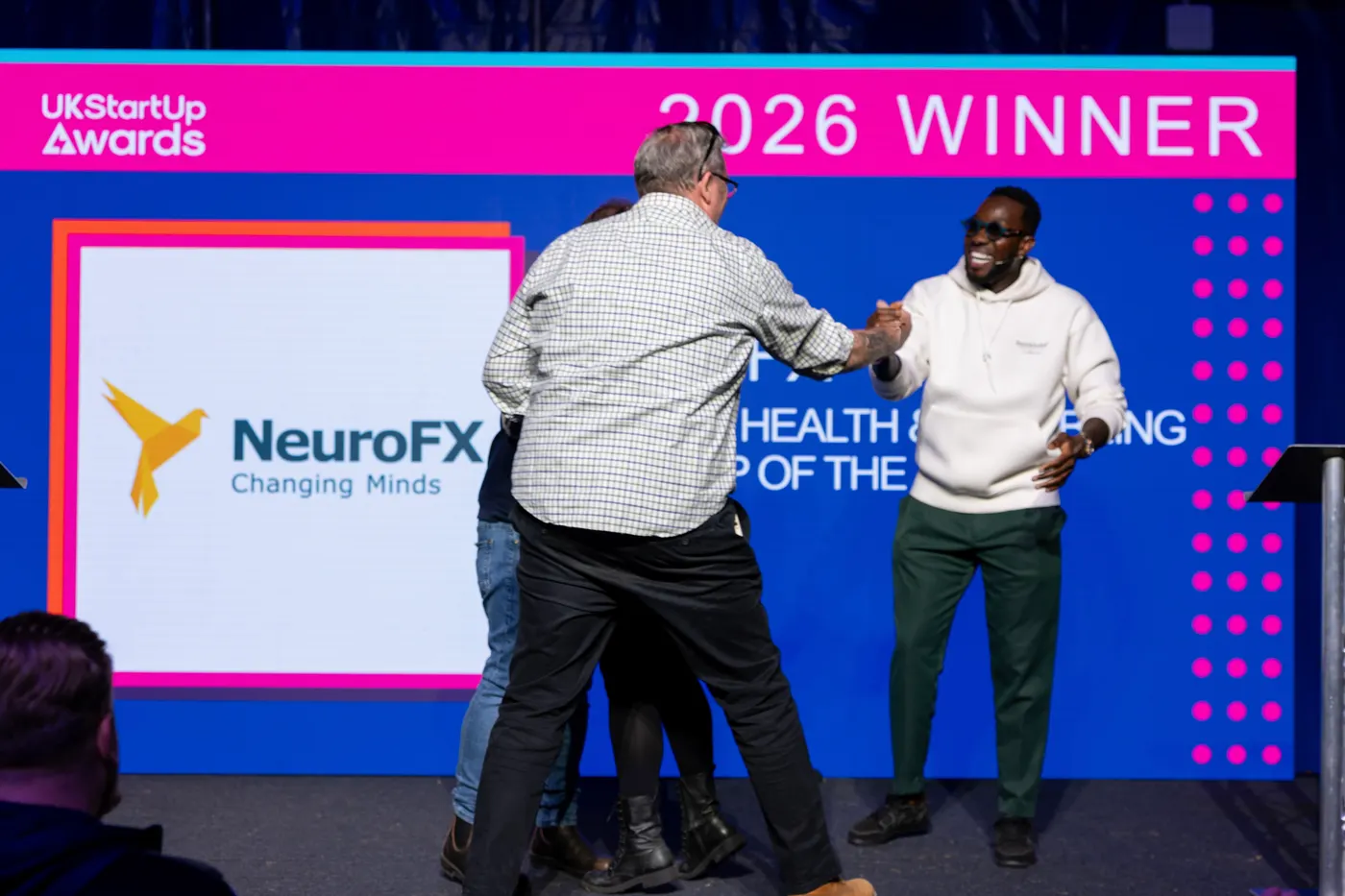 Paul shaking hands with one of the hosts on stage, the NeuroFX Changing Minds logo on the big screen