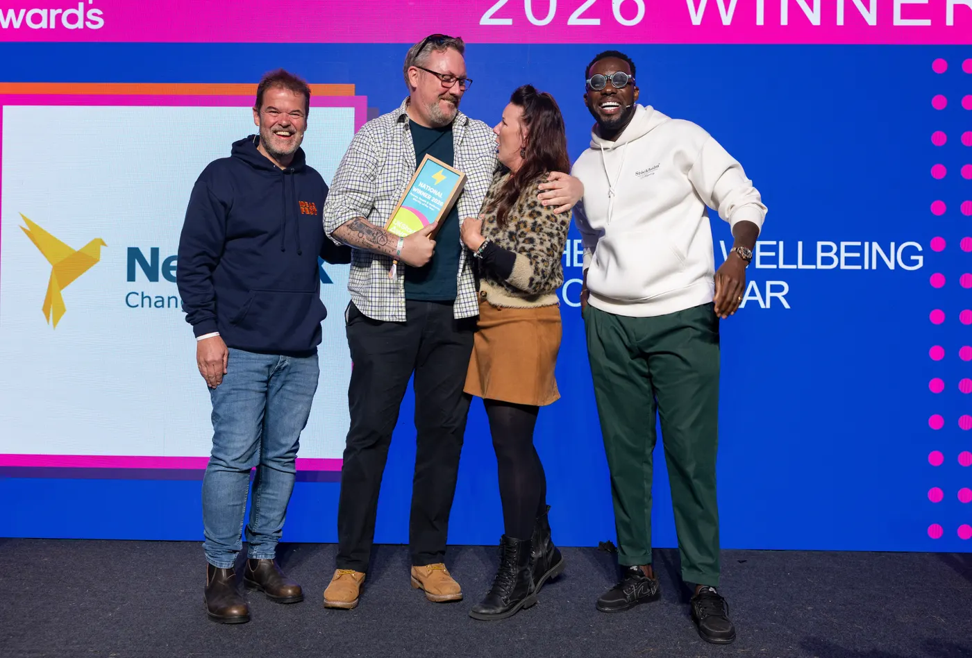 Tina and Paul Fox on stage with the National Winner 2026 certificate, flanked by the evening's hosts, the NeuroFX logo on the screen behind