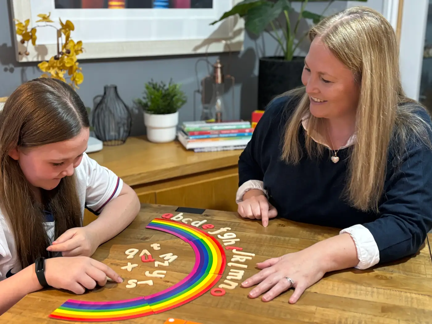 Louise Cunningham working through letter sounds with a pupil, using a rainbow alphabet arc laid out on the table