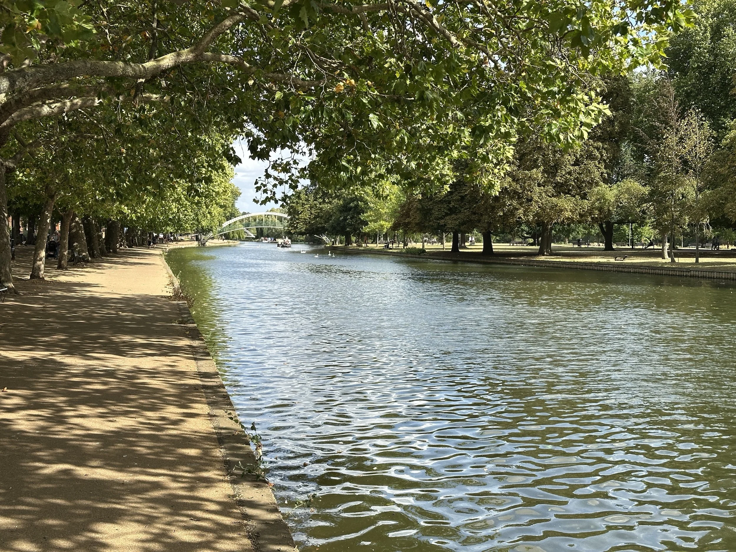 The tree-lined river embankment in Bedford on a bright summer day, with a footbridge in the distance